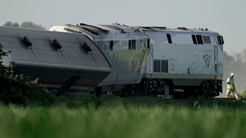 FILE - A worker inspects the scene of an Amtrak train that derailed after striking a dump...